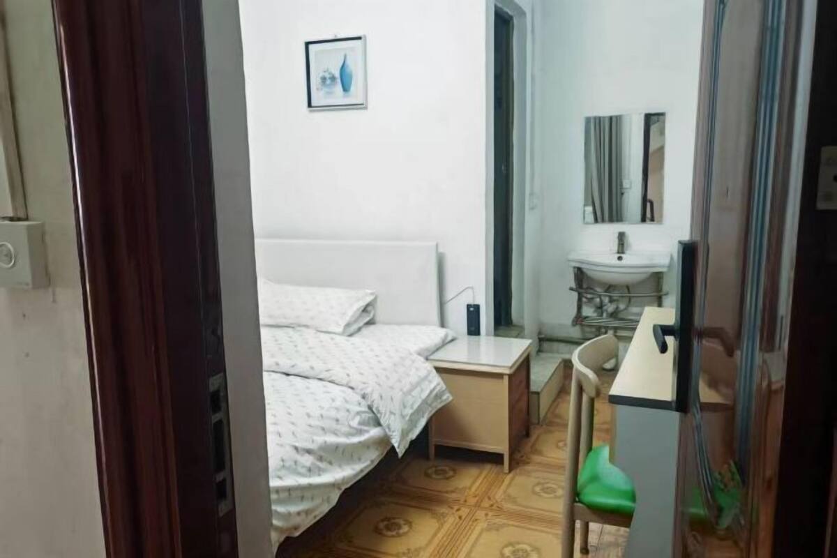 Un dormitorio con cama, mesita de noche, silla, una pequeña mesa, espejo y lavamanos.