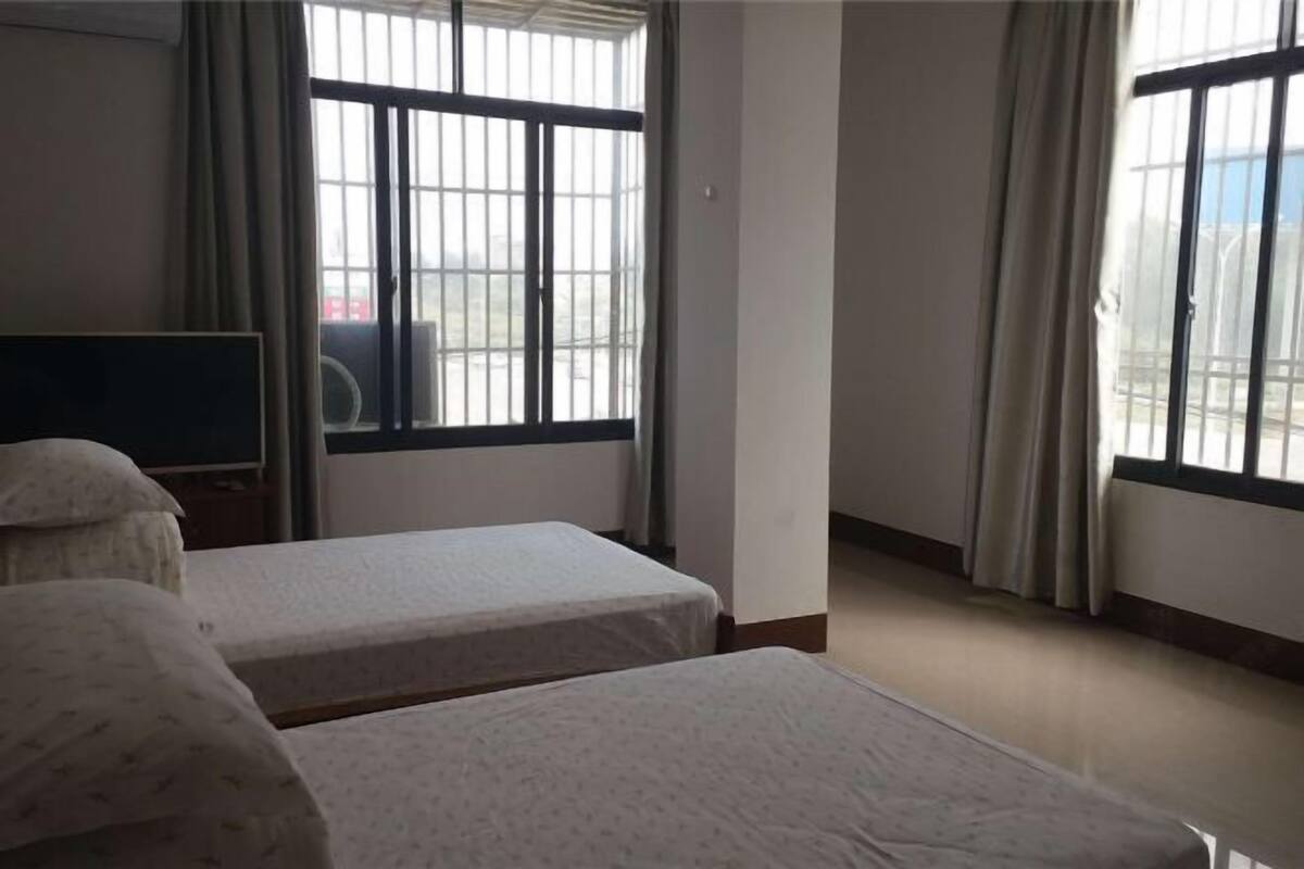 Una habitación con dos camas, televisión y ventanas grandes con cortinas.