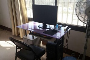A computer desk with a monitor, keyboard, and mouse, a chair, and a standing fan.