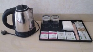 Een roestvrijstalen waterkoker, twee glazen bekers, een dienblad met theezakjes, een zakje suiker en een pakje melk.