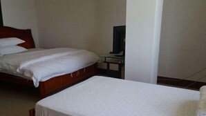 Een hotelkamer met twee eenpersoonsbedden, een kleintje tafeltje en een televisie, en eenvoudige wanden.