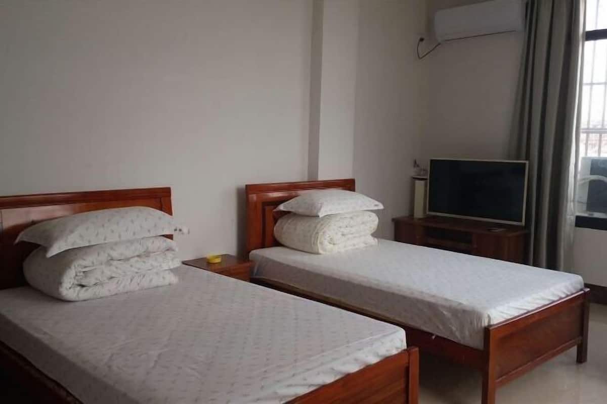 Habitación de hotel con dos camas individuales, televisión y ventana con cortinas.