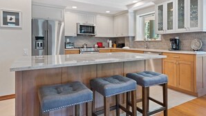 A modern kitchen with a large island, stainless steel appliances, wooden cabinets, and a glass-fronted cabinet. - Beaver Creek Village 2 Bedroom Residence With Ski In/out Access and Pool (Avon)