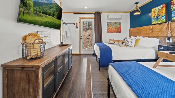 Une chambre d’hôtel moderne dotée d’une grande télévision, d’un lit, d’un bureau et offrant une vue sur une forêt grâce à une porte vitrée.