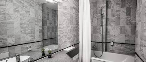 A modern bathroom with marble tiles, a bathtub, a shower, and a sink with two mirrors.