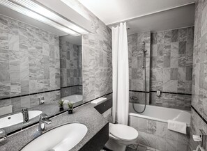 A modern bathroom with marble tiles, a bathtub, a shower, and a sink with two mirrors. - Hotel Mirage Düsseldorf-Neuss (Neuss)