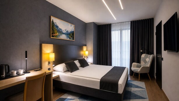 A modern hotel room with a bed, desk, chair, and a painting on the wall. - Hotel Mirage Düsseldorf-Neuss (Neuss)