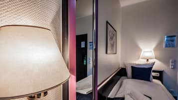 Ein Hotelzimmer mit Bett, Nachttisch, Lampe, Spiegel und einem Wandbild.