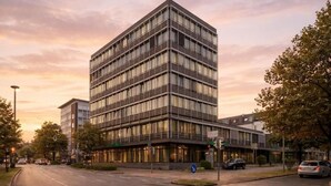 A modern multi-story building with a glass facade, located at a street corner with a clear sky. - Hotel Mirage Düsseldorf-Neuss (Neuss)