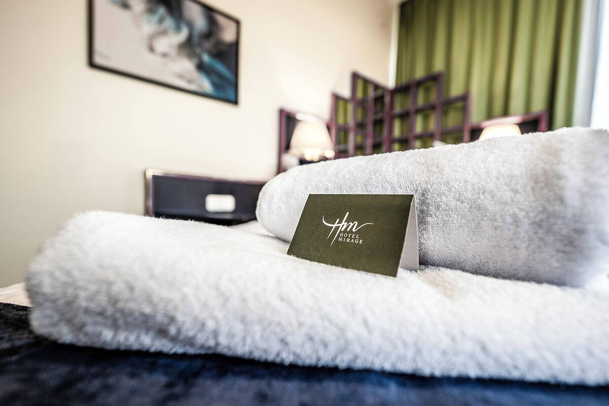 Una cama bien hecha con un edredón blanco mullido y una tarjeta que dice "Hotel Mirage".