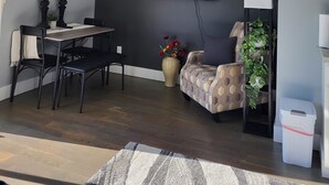 A modern living room with a dark gray accent wall, a flat-screen TV mounted above a wooden dining table, and a patterned armchair. - Our 2nd Studio at The Lofts in Hesperia.
 (Hesperia)