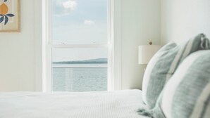 Une chambre dotée d’une grande fenêtre donnant sur un plan d’eau et sur des collines lointaines.