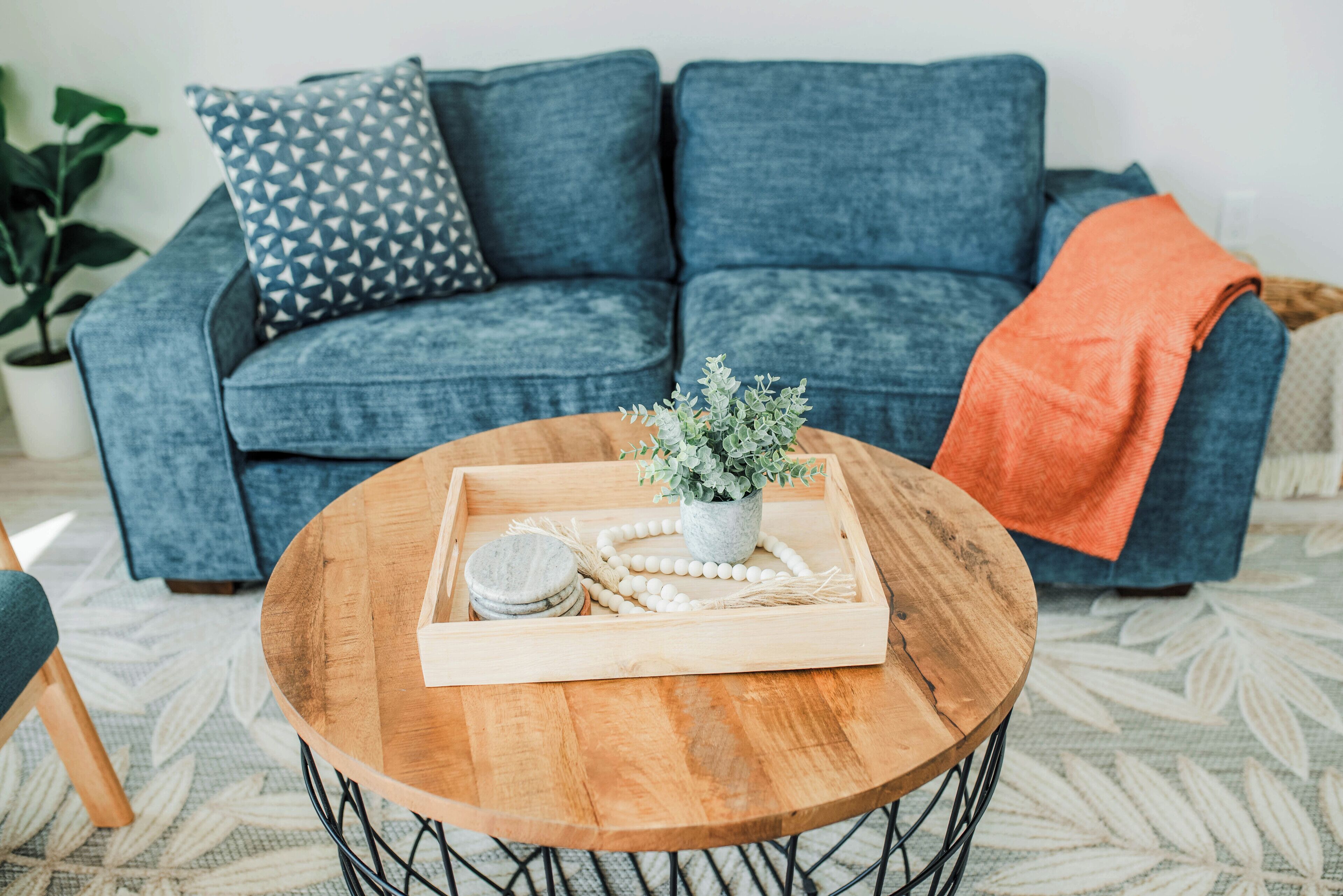 A cozy living room with a blue sofa, a wooden coffee table, and a decorative tray with a plant and beads.