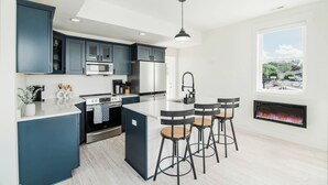 Une cuisine moderne avec des meubles de couleur bleu foncé, un îlot central, des tabourets de bar, un four encastré et une cheminée.