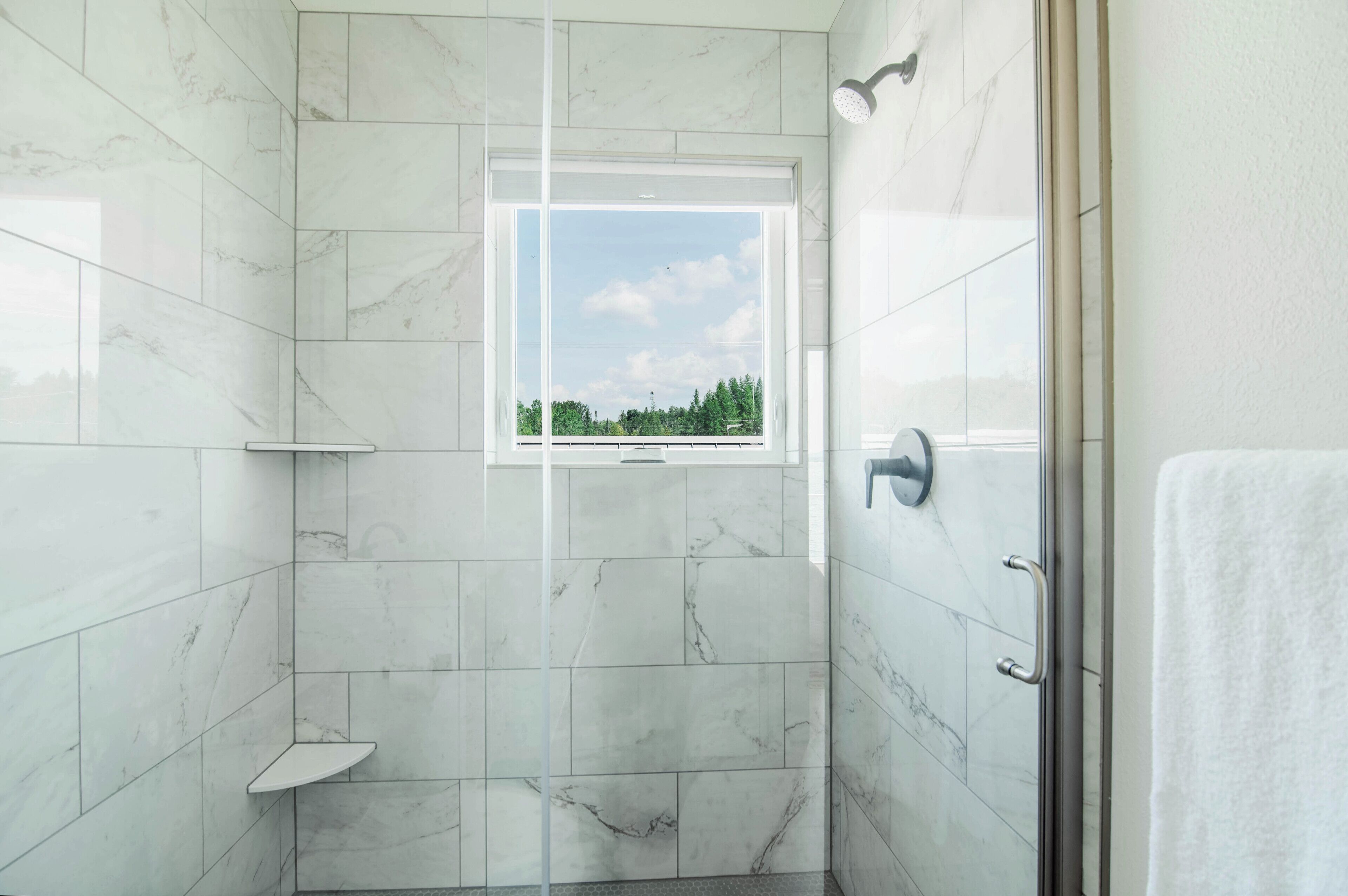 A bathroom with marble tiles, a window, and a shower area.