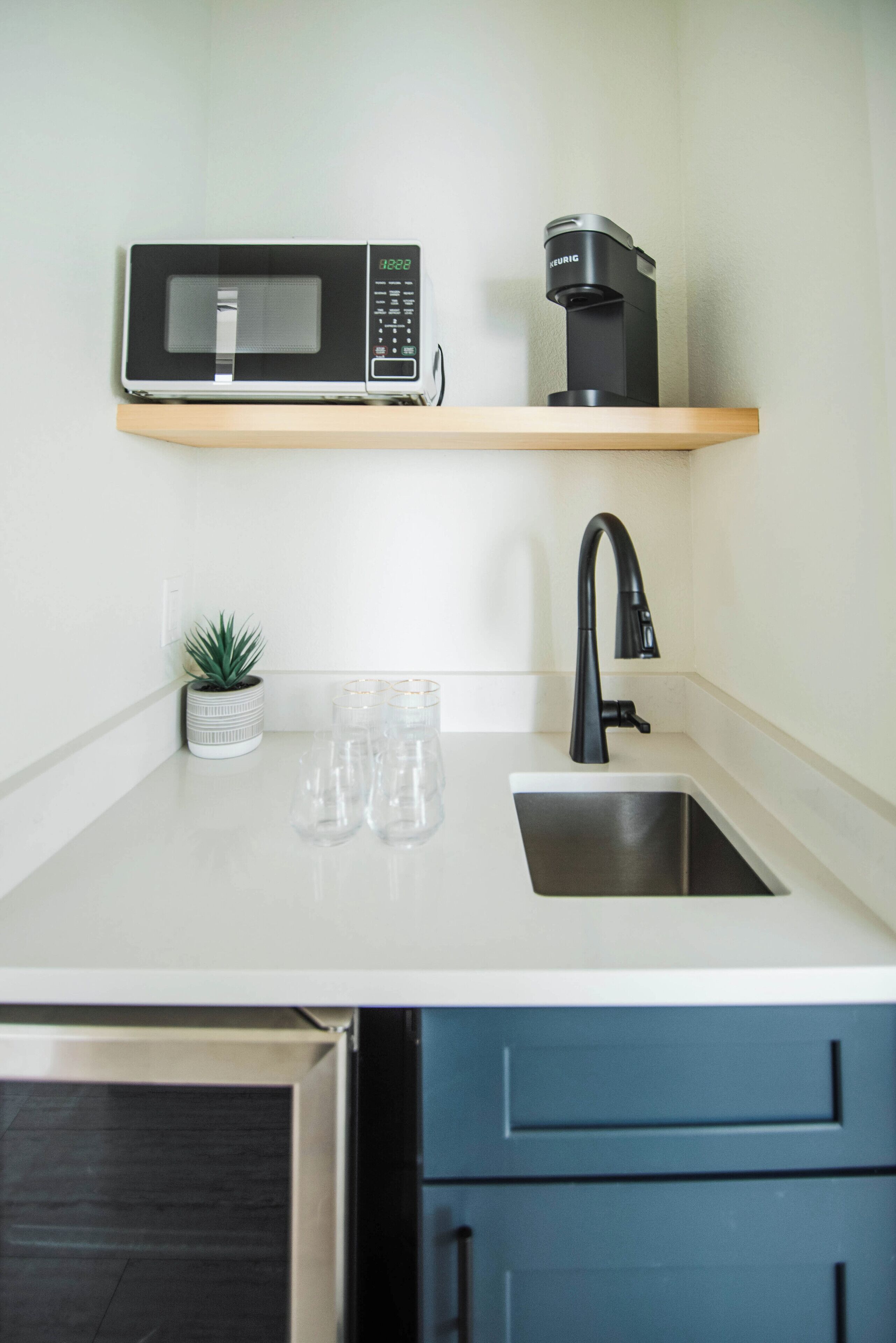 A kitchen with a microwave, coffee maker, sink, and a small potted plant.