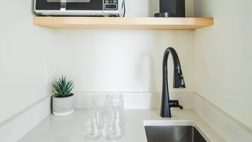 A kitchen with a microwave, coffee maker, sink, and a small potted plant.