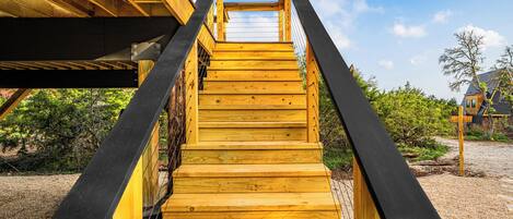 A wooden staircase leading to a covered area with a clear view of the sky and surrounding greenery.