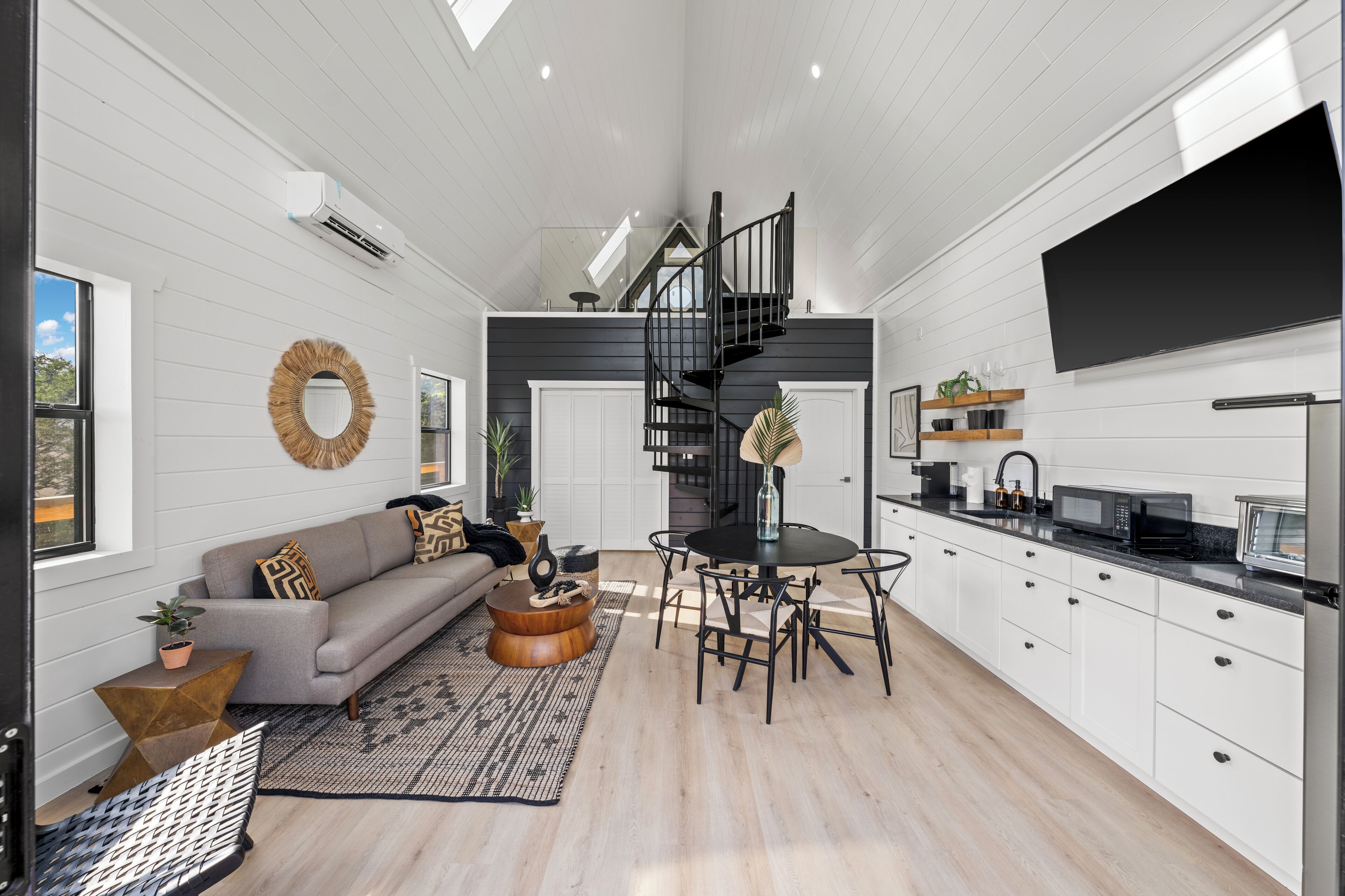 A modern kitchen with white cabinets, a black staircase, and a dining area with a round table and chairs.