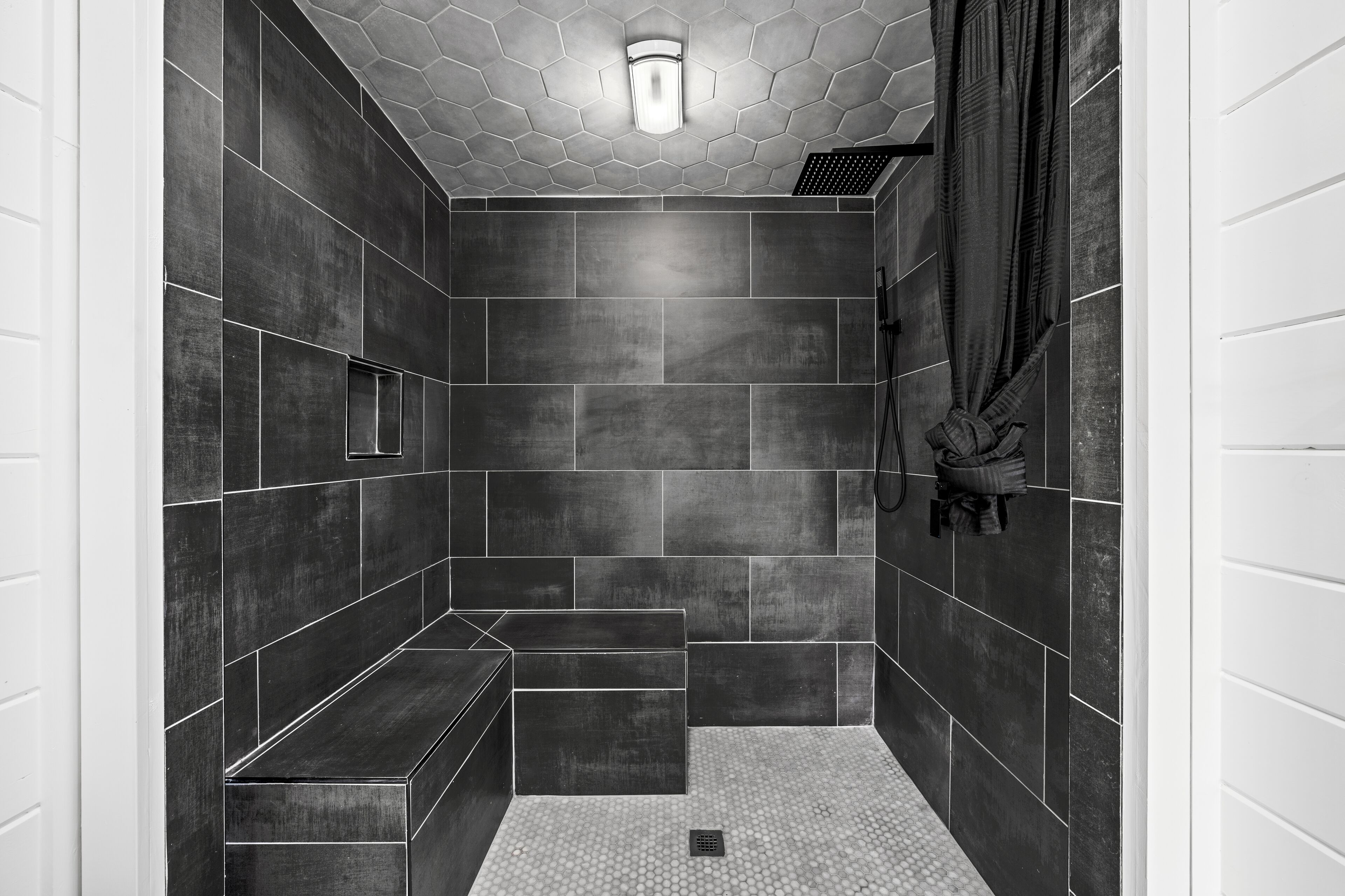 A modern shower area with dark tiles, a hexagonal ceiling design, and a built-in bench.
