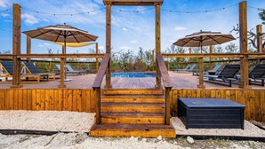 Eine Holzterrasse mit Pool, Liegestühlen und Sonnenschirmen.
