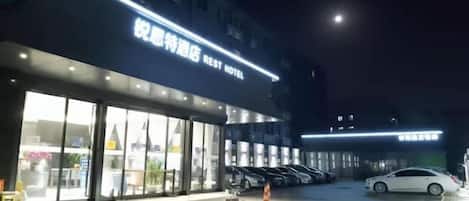 A hotel entrance with a sign reading "Rest Hotel" and a parking area with several cars.