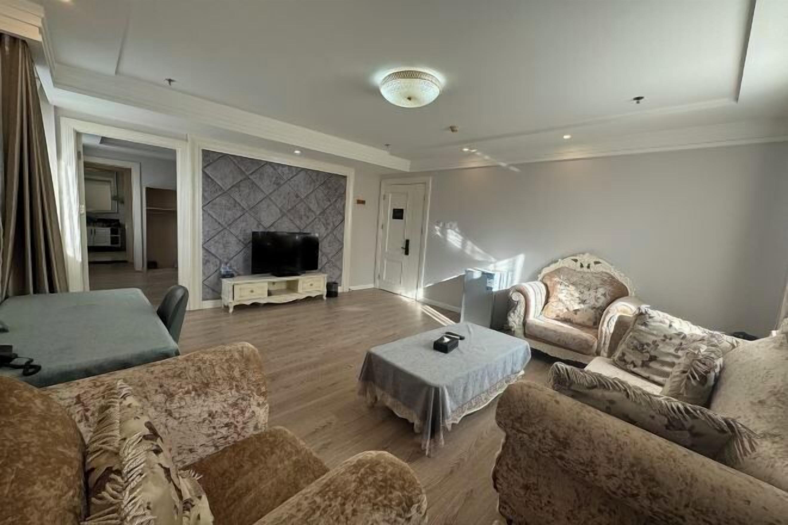 A living room with a television, a sofa, a coffee table, and a patterned wall.