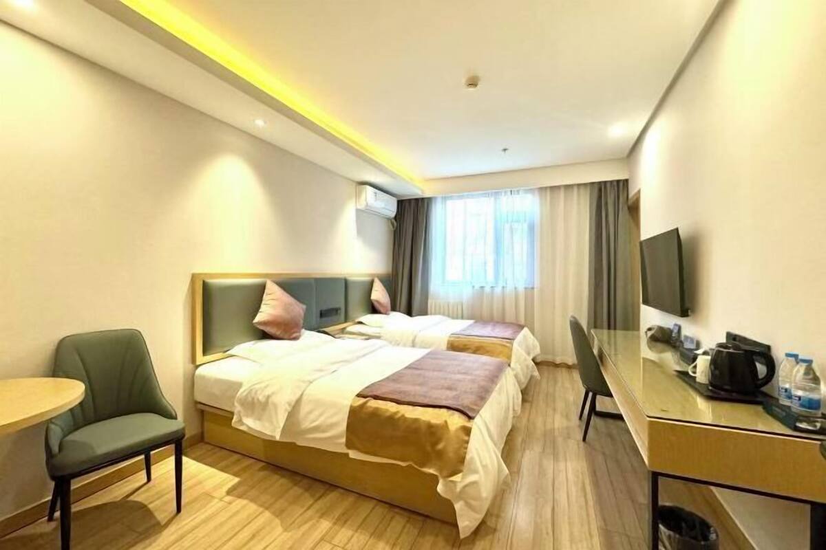 A hotel room with two beds, a desk with a chair, a small table, and a TV.
