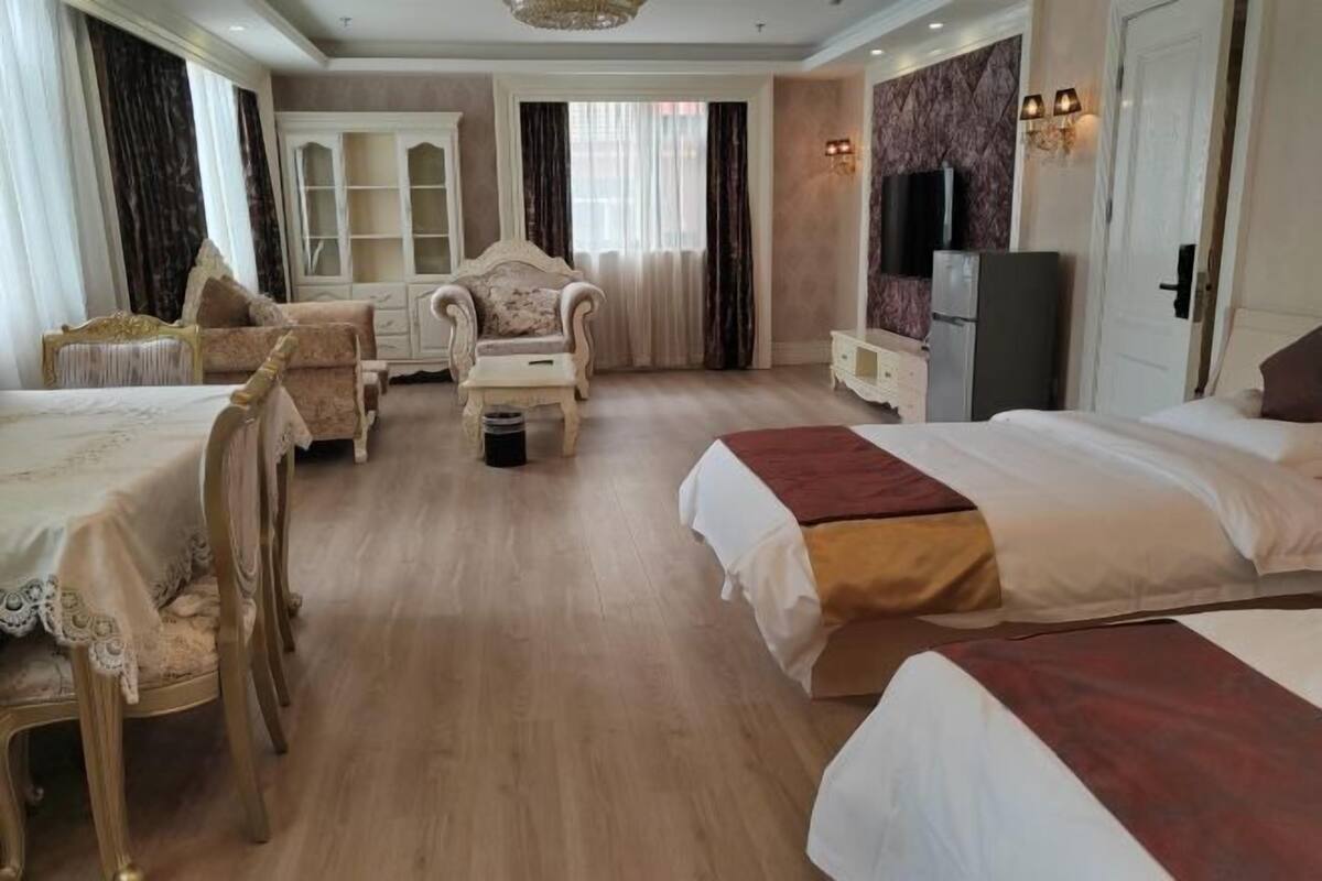A hotel room with two beds, a dining table, a sofa, a cabinet, and a television.