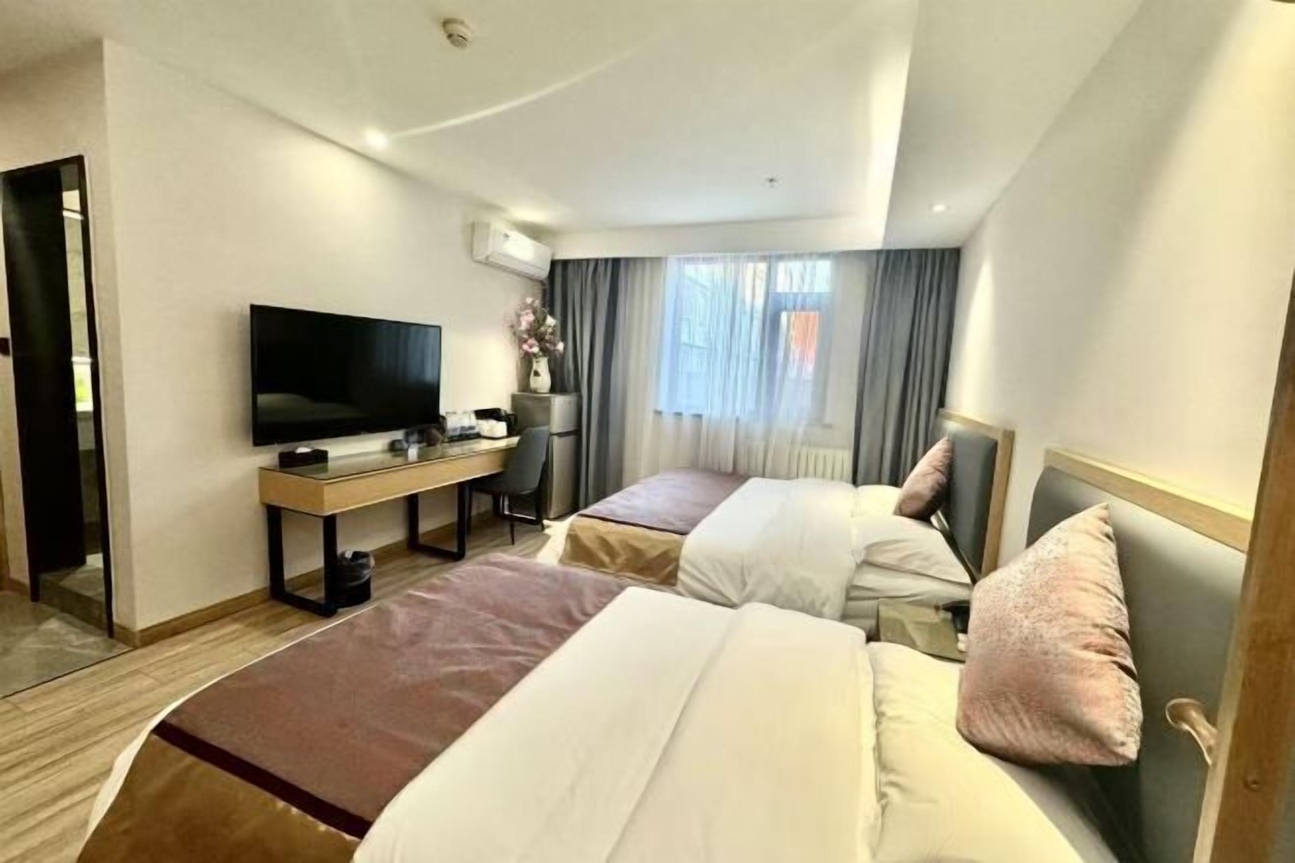 Habitación de hotel con dos camas, un escritorio con televisor y un ventanal con cortinas.