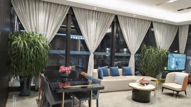 Uma sala de estar moderna com um sofá, cadeiras, uma mesa de centro e janelas amplas com cortinas.