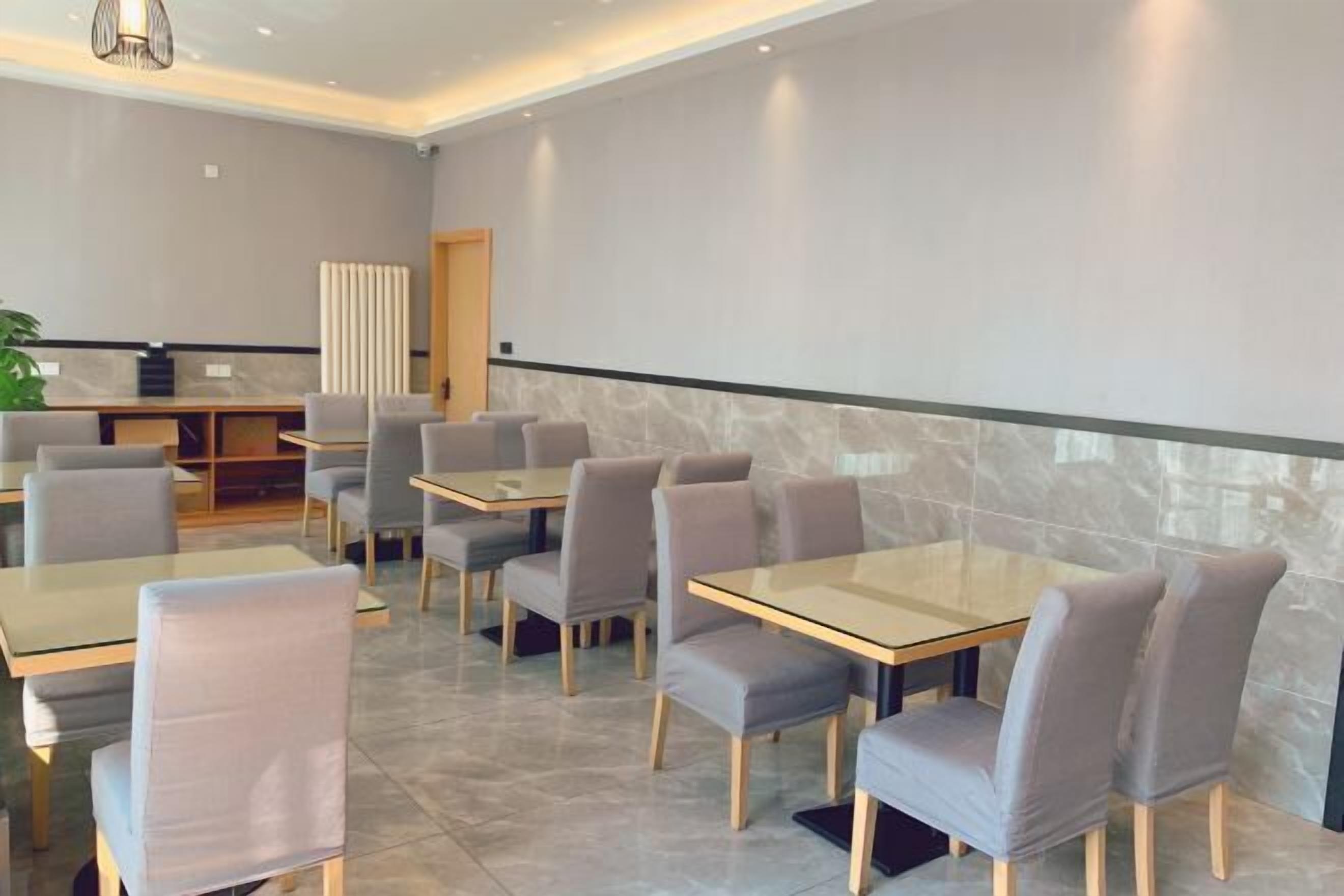 A modern restaurant with a clean, minimalist design, featuring grey upholstered chairs and rectangular tables.