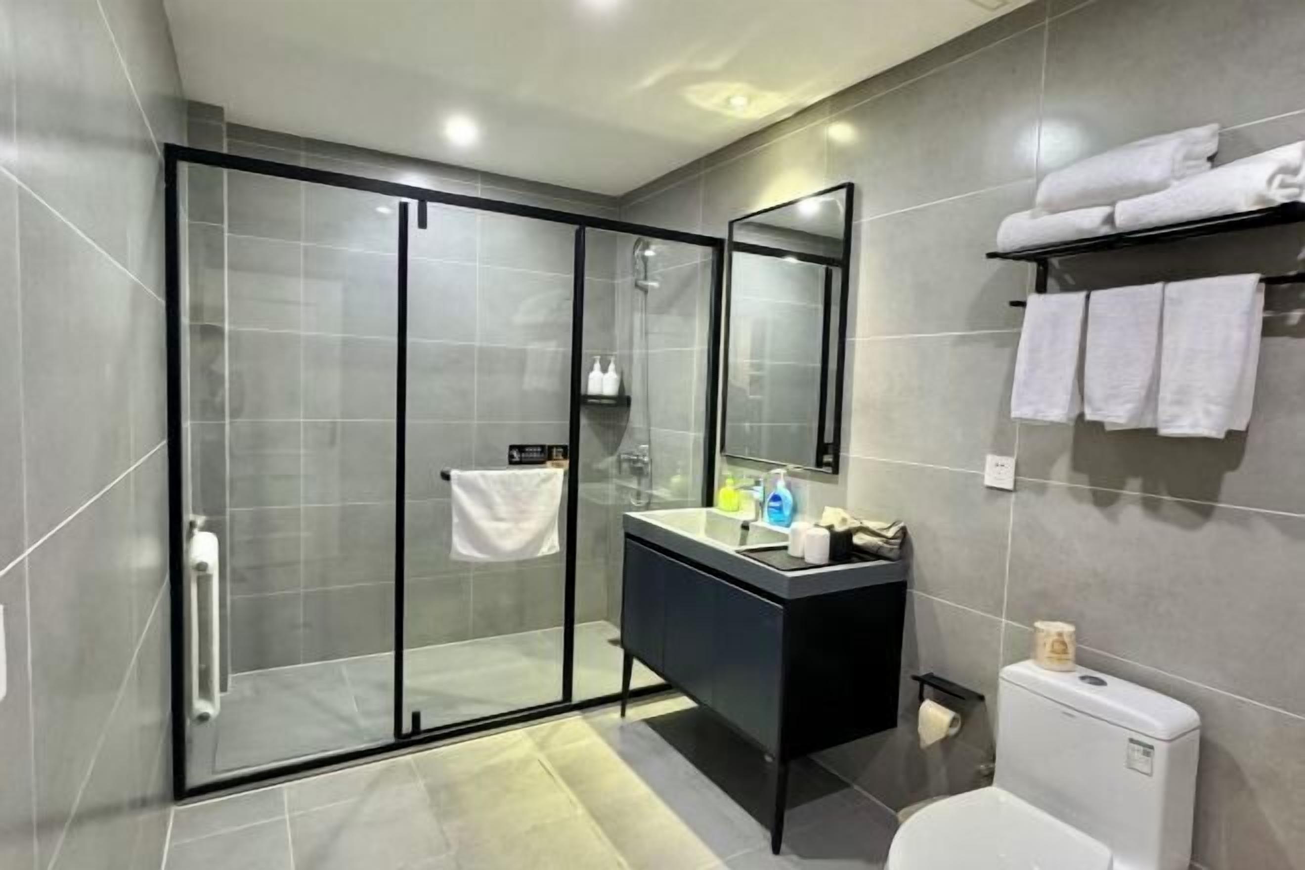 Et moderne badeværelse med en glasbrusekabine, en sort kommode og et toilet.