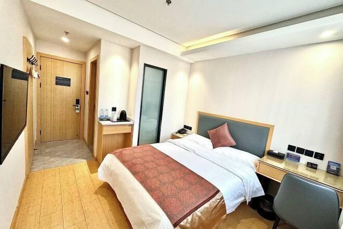 A hotel room with a bed, desk, chair, and a small bathroom area.