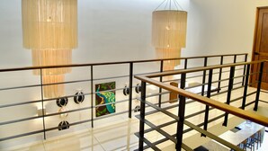Un intérieur moderne avec une balustrade en verre, un tableau représentant un paon et deux grands luminaires cylindriques.