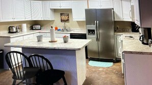 Una cocina con gabinetes blancos, un refrigerador de acero inoxidable, una cafetera y dos sillas negras.