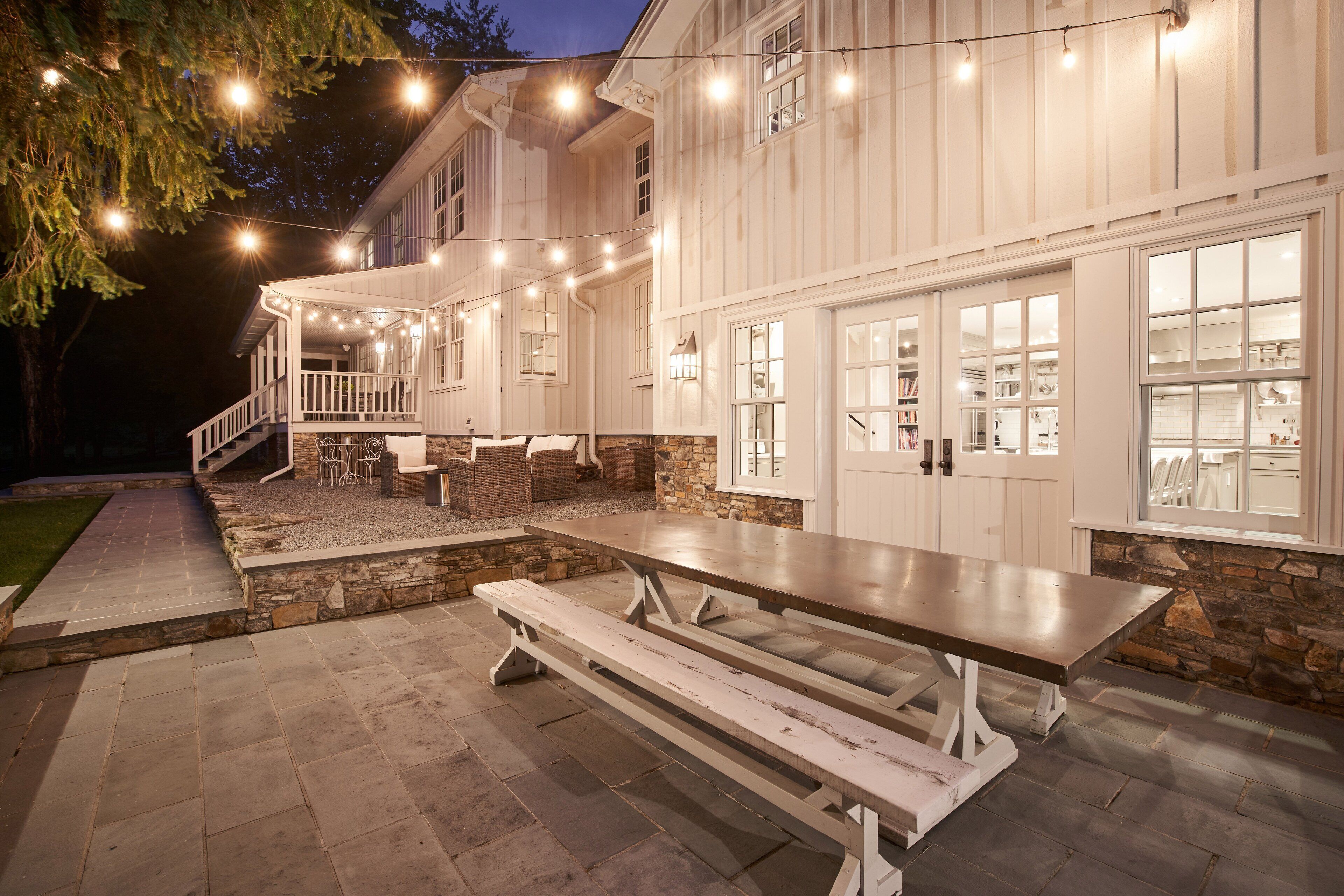 A large outdoor dining area with a picnic table and benches, surrounded by stone walls and a wooden deck.
