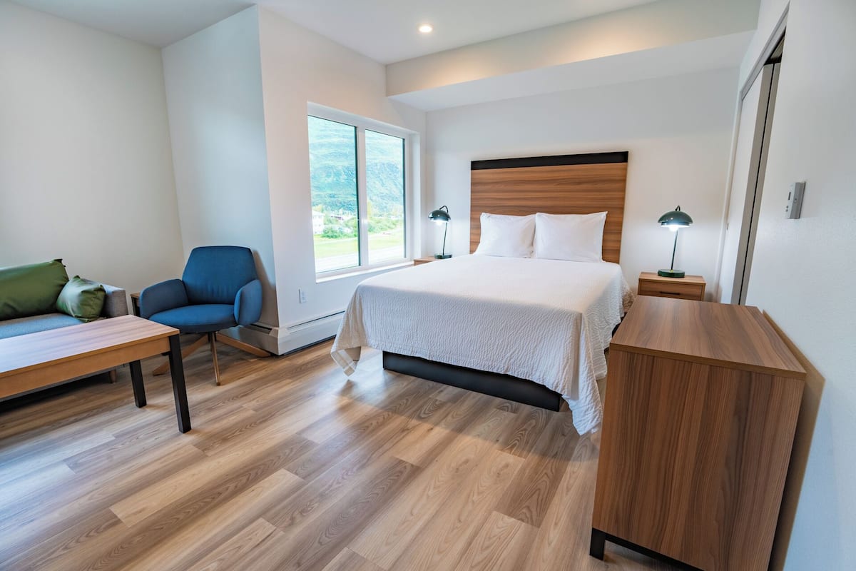 A modern bedroom with a large bed, a desk, a chair, and a nightstand.