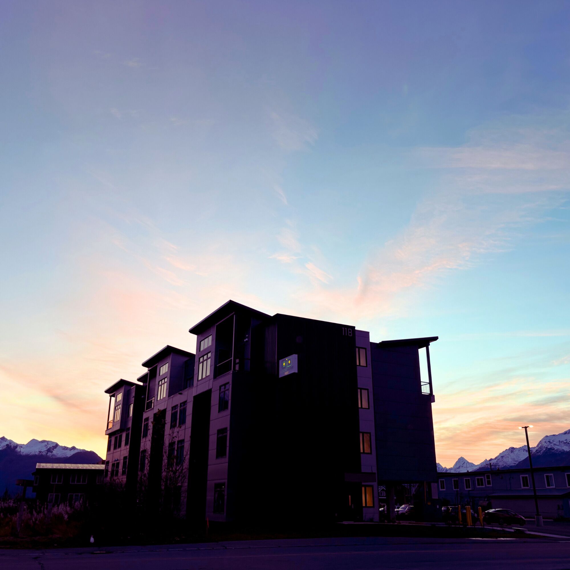 Un edifici de diversos pisos amb teulada plana, probablement un hotel o complex d'apartaments, amb una vista de muntanyes nevades al fons.