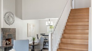 A modern living room with a stone fireplace, a grey sofa, and a wooden staircase.