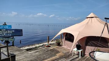 A tent on a wooden deck by a calm body of water, with a sign indicating a lane and a warning about using personal watercraft.