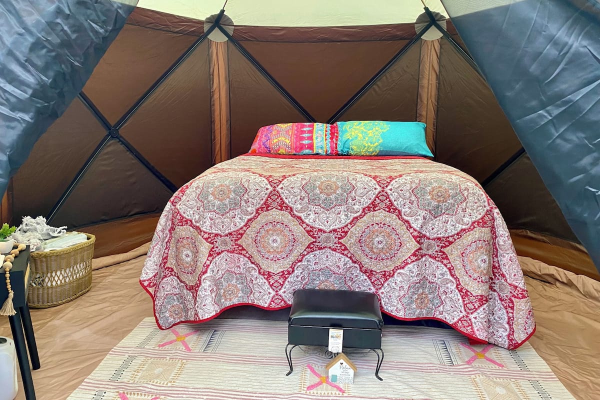 A tent with a bed, pillows, a small bench, and a decorative item on the floor.