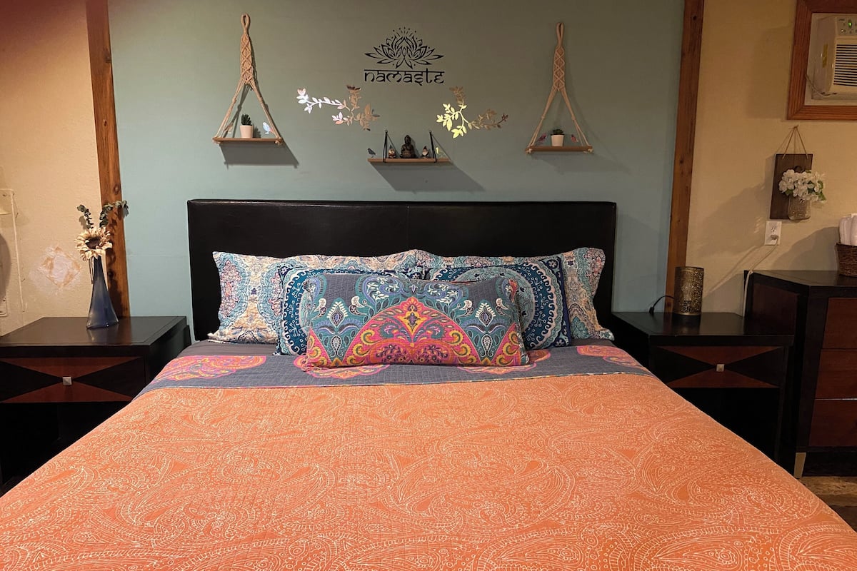 A bed with patterned bedding, a dark headboard, and decorative wall hangings.