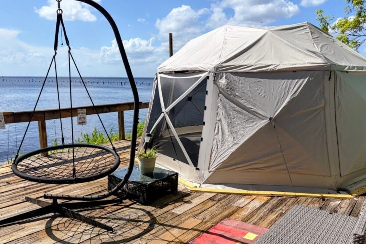 A tent on a wooden deck with a hanging chair and a small potted plant.