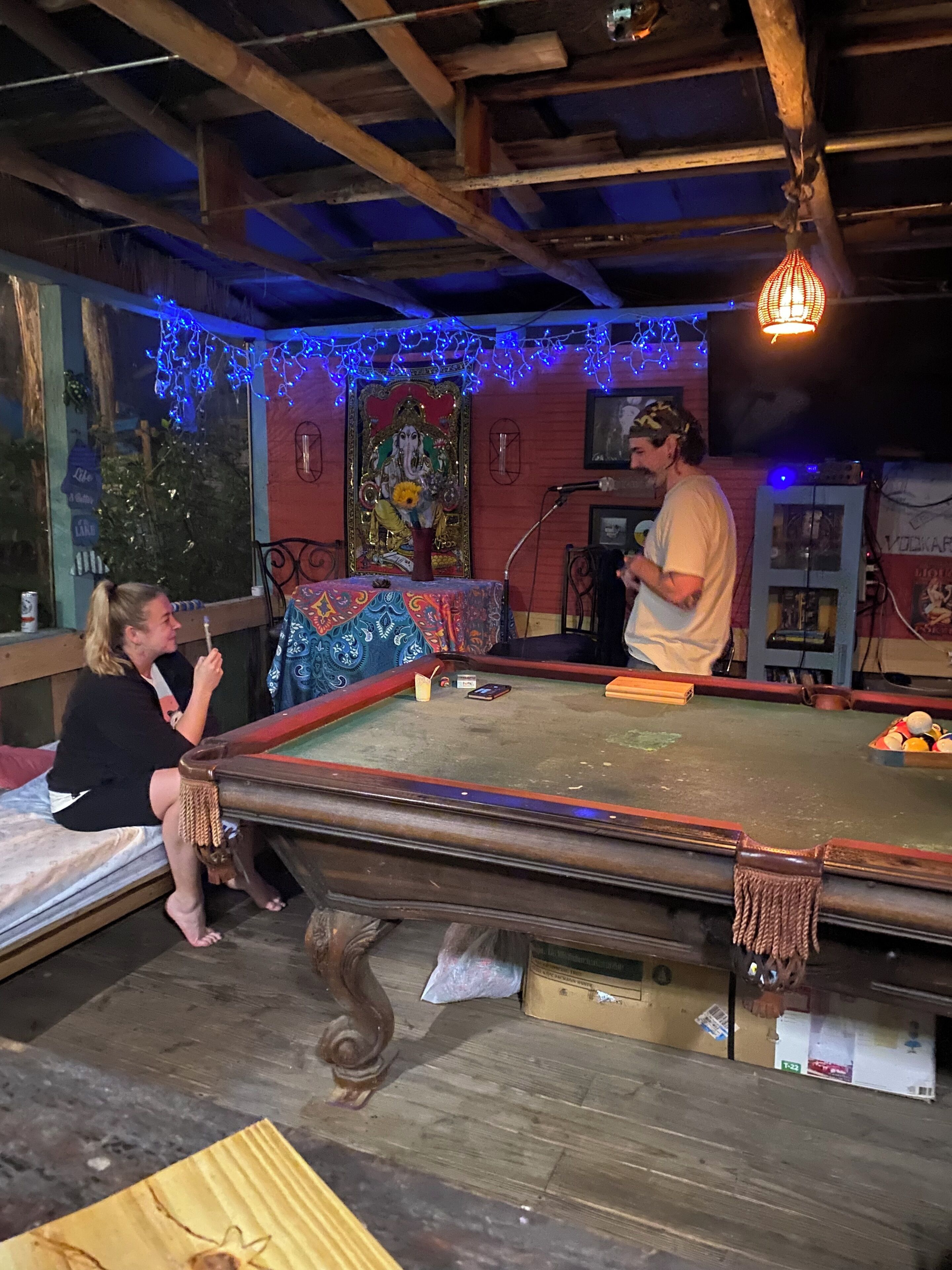 A billiards table with a pool cue and balls, a person playing, and another person sitting on a bench.