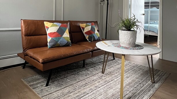Un salon moderne avec un canapé en cuir marron, une table ronde blanche et une plante en pot.