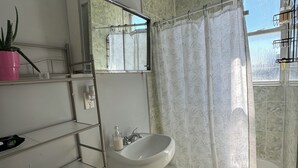 Une salle de bain avec un lavabo blanc, un miroir, des toilettes, un rideau de douche et une fenêtre.