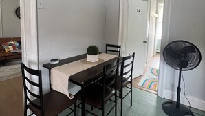 Un coin repas comprenant une table, des chaises, une petite plante en pot et un ventilateur sur pied.