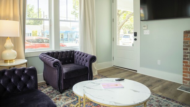 Ein Wohnzimmer mit einem gepolsterten Sessel, einem runden Couchtisch und einem an der Wand befestigten Fernseher.