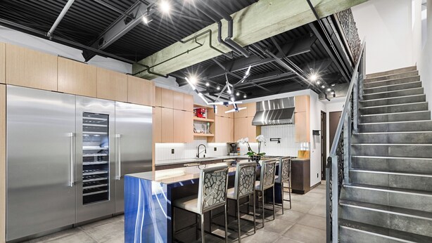 Una cocina moderna con electrodomésticos de acero inoxidable, una isla central con taburetes y una escalera que sube a otro nivel.